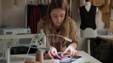 Bir terzi dikiş makinesinin yanındaki kumaş örneklerini inceler.