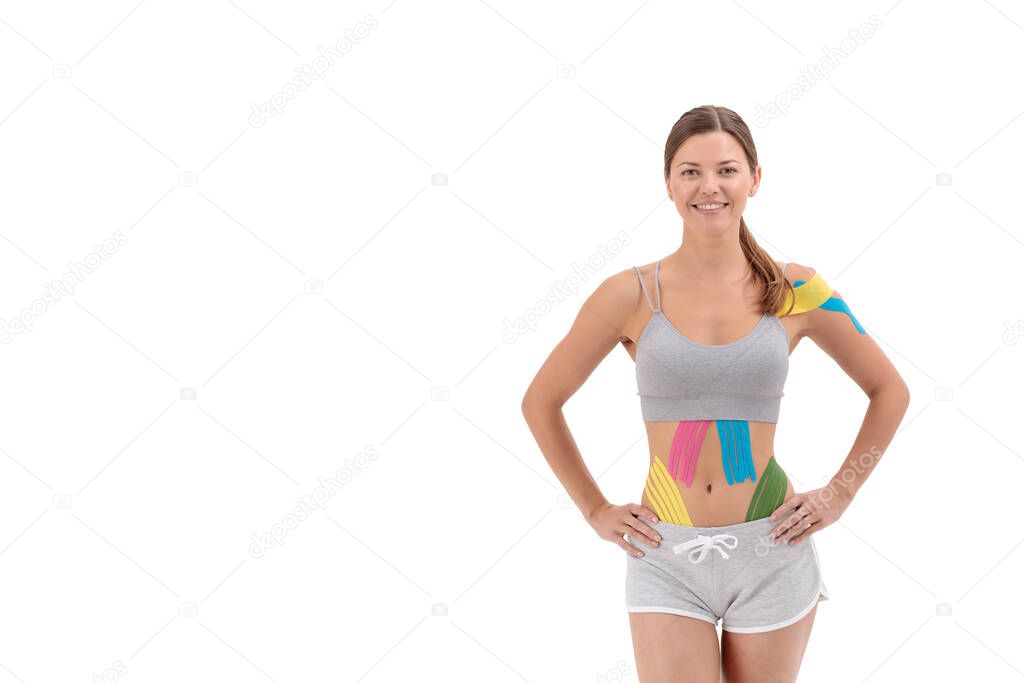 Kinesiology taping. Young female athlete isolated on white background with kinesiology tape on belly and shoulder. Fat lose, cellulite removal, sport physical therapy, recovery concept. Copy space