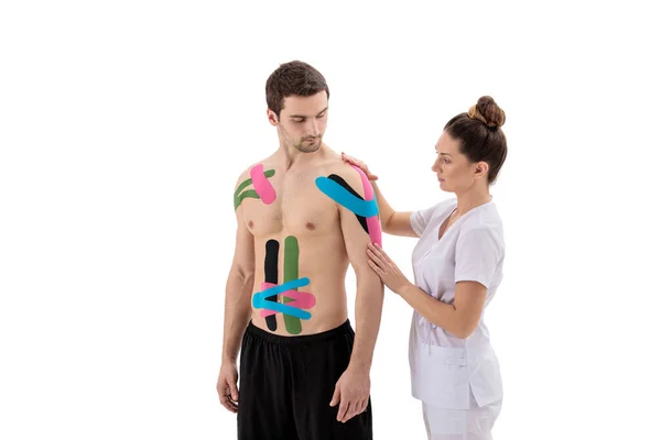 女性理疗师在白色背景下隔离的病人肩部贴上运动胶带 — 图库照片