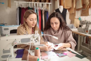 Tasarımcılar elleriyle bir stüdyonun dikiş makinesinin yanında numune kumaşı inceliyorlar.