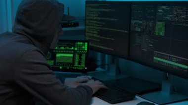 Kapüşonlu sweatshirt giyen bilgisayar klavyesine yazı yazan ve şifreyi kıran tanınmamış bir hacker. Tehlikeli kapüşonlu bilgisayar korsanının yan görüntüsü.