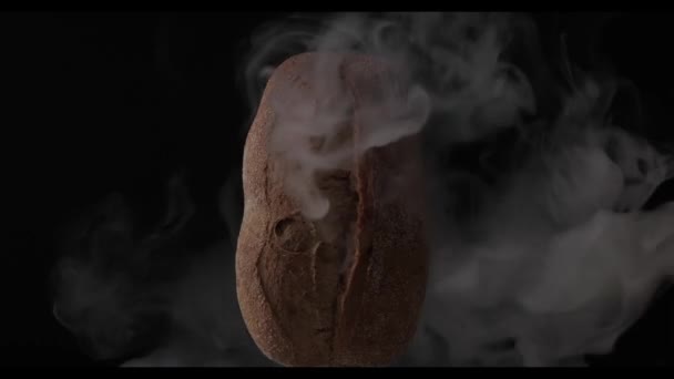 Домашний свежий темный буханка хлеба в дыму на черном фоне — стоковое видео