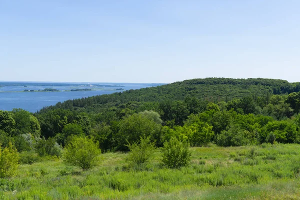 Çok güzel bir panoramik yaz manzarası. Parlak yeşil tarlalar, yoğun orman ve berrak bir gökyüzünün altında büyük bir nehrin ya da gölün sakin mavi suları.