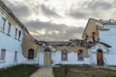 Tarihi bir binanın merkezi savaş yüzünden tamamen harap olmuştur. Çökmüş bir çatı, açık tuğla ve dramatik bir gökyüzü altında boş kemerli pencere çerçeveleri gösterilmiştir.