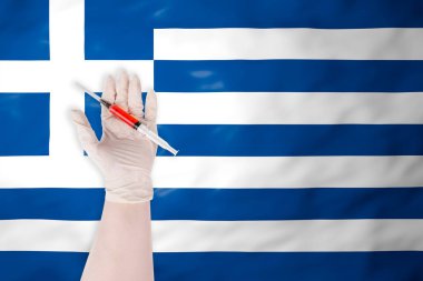 Yunanistan 'ın sallanan bayrağına kırmızı sıvıyla bir şırınga tutan koruyucu eldivendeki el aşı ve tıbbı sembolize ediyor.