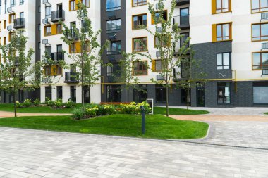 Çağdaş, çok katlı bir apartmanın dış cephesi. İyi korunan avluda yaşayanlar için yemyeşil çimenler, dekoratif çalılar, genç ağaçlar ve taş kaldırımlar yer alıyor.