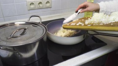 Kadın elleri sotelenmek için yağlı tavaya tahta bir tahtadan doğranmış soğan ekliyor. Mutfakta ev yapımı çorba hazır.