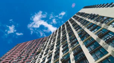Mavi gökyüzüne karşı modern apartmanın alçak açılı görüntüsü. Beyaz bulutların zaman çizelgesi şehirdeki yüksek binaların üzerinden hızla geçiyor.