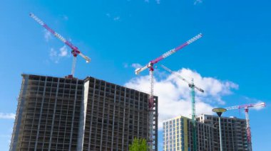 Yeni apartmanların şantiyesindeki vinçlerin zaman çizelgesi. Mavi gökyüzünün altında hareket eden bulutlarla modern yerleşim alanının gelişimi