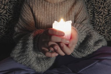 Karanlık bir odada parlayan bir mumu tutan kadın ellerini kapat. Umut kavramı, sıcaklık ve rahat atmosfer.