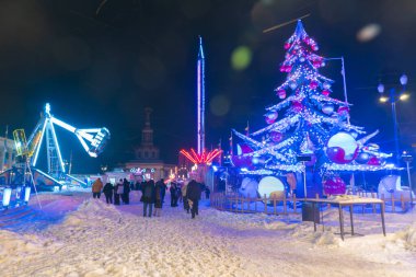 Ukrayna, Kyiv - 02.08.2026: İnsanlar kış gecesi aydınlanmış Noel ağacı ve atlıkarıncayla lunaparkta yürüyorlar. Neon ışıkları ve karlı tatil ortamı