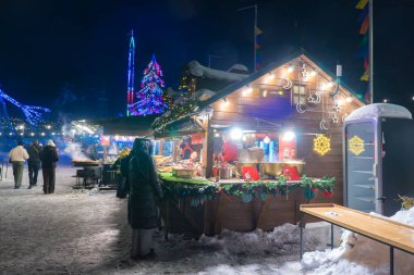 Ukrayna, Kyiv - 02.08.2026: Geceleri rahat ahşap gıda tezgahları, şenlikli tel lambaları, parıldayan dekoratif tesisatı ve karlı bir parkta yürüyen insanlarla birlikte kış pazarı