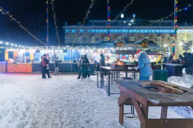 Ukrayna, Kyiv - 02.08.2026: Geceleri rahat ahşap gıda tezgahları, şenlikli tel lambaları, parıldayan dekoratif tesisatı ve karlı bir parkta yürüyen insanlarla birlikte kış pazarı