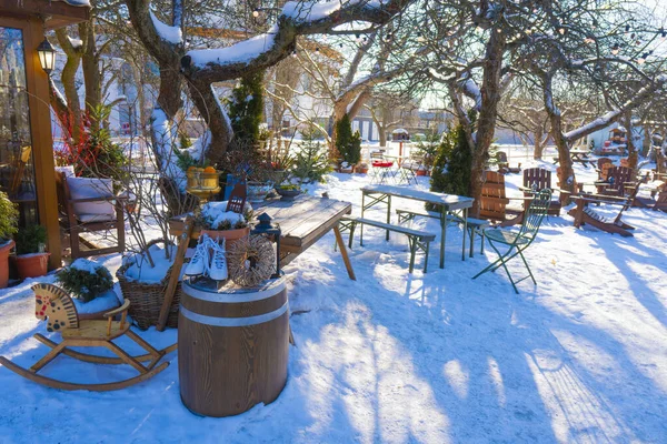 Karlı bir kış bahçesinde, rahat bir kafeterya terasında ahşap masalar, sandalyeler, beyaz buz patenleri ve parlak güneş ışığı altında sallanan bir at.