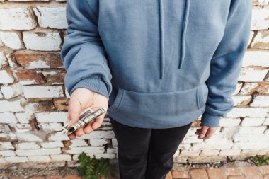 Mavi kapüşonlu zavallı bir kızın elinde katlanmış bir dolar banknotuyla yakın plan fotoğrafı. Yoksullara sosyal eşitsizlik, yoksulluk ve mali yardım kavramı