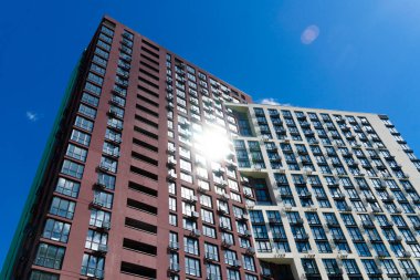 Çağdaş meskun gökdelenlerin alçak açılı görüntüsü. Açık mavi gökyüzüne karşı cam pencerelere yansıyan güneş. Modern şehir mimarisi