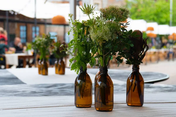 Küçük narin buketler yabani çiçekler ve kehribar camlı eczane şişeleri açık hava yaz kafesinde bulanık bir arka planda beyaz bir masada.
