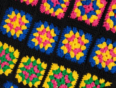 Brightly colored crocheted granny squares are laid out on the surface. The vibrant color palette of fuchsia, yellow, and blue contrasts sharply with the black connectors.