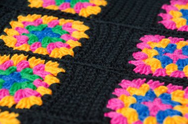 Brightly colored crocheted granny squares are laid out on the surface. The vibrant color palette of fuchsia, yellow, and blue contrasts sharply with the black connectors.