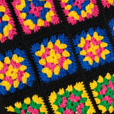 Brightly colored crocheted granny squares are laid out on the surface. The vibrant color palette of fuchsia, yellow, and blue contrasts sharply with the black connectors.