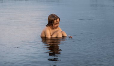 Genç bir çocuk, göl yatağında dinlenerek ve yaz boyunca sakin sularla çevrili sakin bir anın tadını çıkarır..