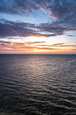 Güneş doğarken denizin üzerinde şafak söküyor, gökyüzünü turuncu ve sarıya boyuyor. Dalgalar yumuşaktır ve İsveç kıyılarında atmosfer taze ve parlaktır..
