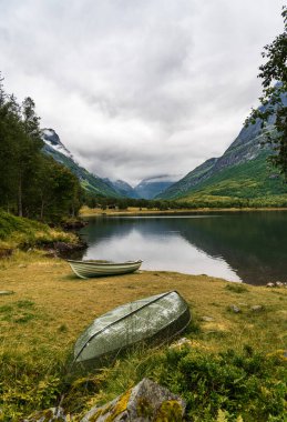 Innerdalen, kıyıda dinlenen iki yalnız sandalla Innerdalsvatna Gölü 'nü gösteriyor. Norveç 'te bulutlu bir gökyüzünün altında Trollheimen dağları yükselir.