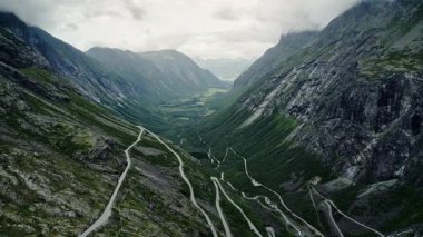 Sinema insansız hava aracı geri çekilirken Trollstigen Yolu ve Isterdalen Vadisi 'nin dolambaçlı olduğu görülüyor. Norveç 'in daha fazla og Romsdal şehrinde, kasvetli bir gökyüzünün altında ziyaretçi merkezi ve engebeli dağların manzarası.