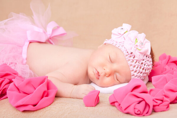 A sleeping newborn baby girl wearing a pink headband and tutu