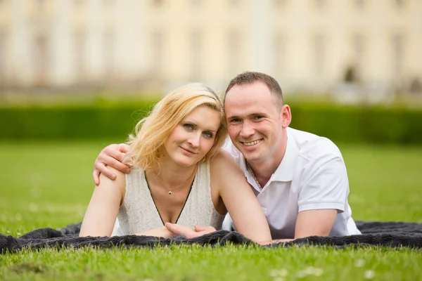Młoda, szczęśliwa i uśmiechnięta para leży na trawie — Zdjęcie stockowe