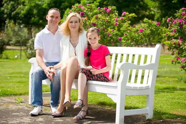 Familia feliz se sienta en un banco en el parque al aire libre — Foto de Stock