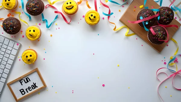 AI celebration flat lay concept showing a colorful festive workspace with cupcakes, smiley face cookies, confetti, ribbons, and decorations arranged around a white background with a keyboard. 
