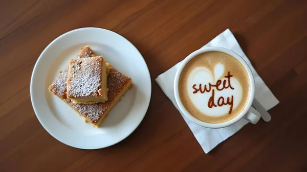 AI coffee and dessert concept showing a cozy caf setup with a cup of latte art coffee and a plate of square cakes dusted with powdered sugar.