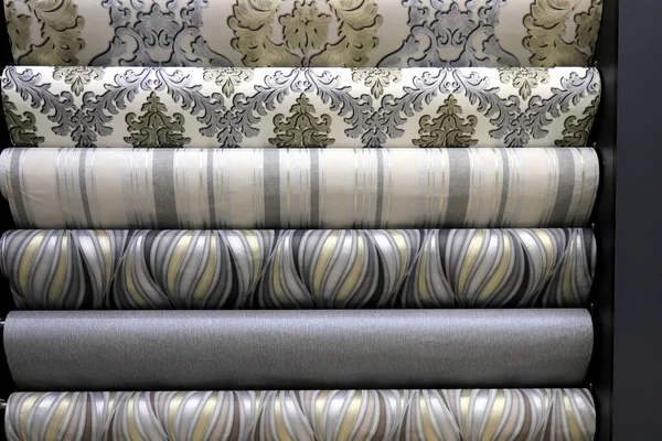 Rolled up rolls of vinyl wallpaper in a building supermarket, shop. Gray, white, beige wallpaper for the wall, decorative finishing materials for the renovation of a room, interior