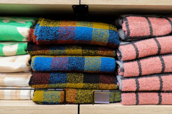 A stack of warm soft, fluffy, wool plaids in a cage lies on a shelf in a wardrobe, store. Blankets for warmth and comfort in the supermarket in red, blue, yellow in winter — Stock Image Stack Warm Soft Fluffy Wool Plaids Cage Lies Shelf Wardrobe Stock Picture