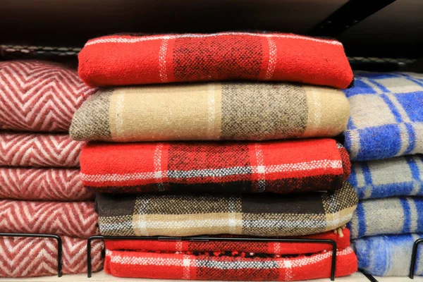 A stack of warm soft, fluffy, wool plaids in a cage lies on a shelf in a wardrobe, store. Blankets for warmth and comfort in the supermarket in red, blue, yellow in winter — Stock Image Stack Warm Soft Fluffy Wool Plaids Cage Lies Shelf Wardrobe Royalty Free Stock Photos