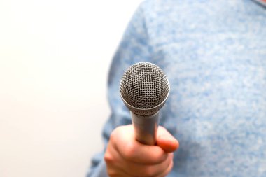 Bir adam elinde gümüş gri bir mikrofon tutuyor ve iş görüşmeleri yapıyor. Gazeteci gazetecilik, halka açık konuşma, basın toplantısı, karaoke söylüyor.
