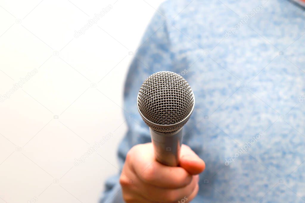 A man holds a silver gray microphone in his hand and conducts business interviews, journalistic reporting, public speaking, press conference, sings karaoke