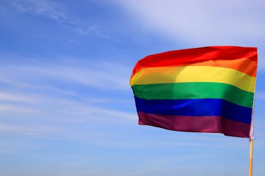 Mavi gökyüzünde gey gökkuşağı bayrağı sallıyor. Lezbiyen, gey, biseksüel, transseksüel insanlar için LGBT topluluğunun parlak bayrağı.