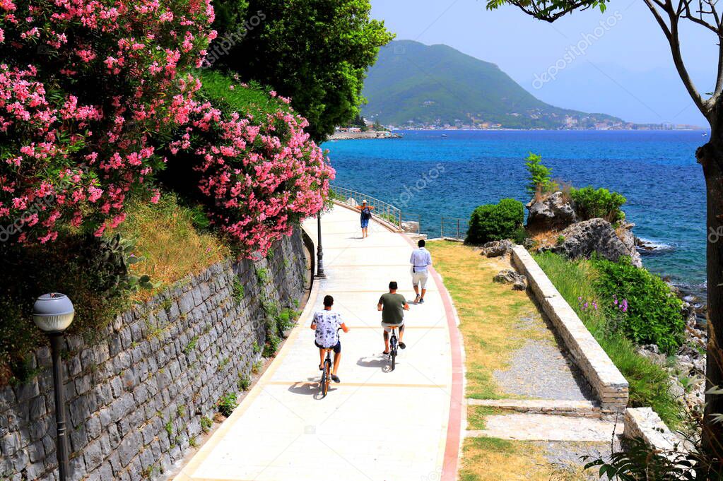 The picturesque city Herceg Novi, Montenegro, in the mountains, shore of Kotor. Scenic summer resort landscape in Herceg Novi. People walk and ride bicycle near the blooming oleander and beach