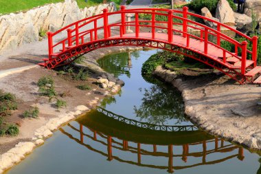 Yeşil bir parktaki küçük bir nehrin karşısındaki eski kırmızı ahşap köprü. Klasik Japon tarzı köprü suya yansıyor. Uman, Ukrayna Yazın, ilkbaharda, sonbaharda.