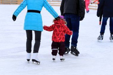 Küçük çocuk kışın buz pistinde paten kayar. Bir erkek ve bir kadın çocuğa paten kaymayı öğretiyor. Spor kulüpleri, aktif aile sporları, Noel kış tatilleri..