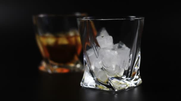 Whiskey wordt gegoten in een glas tegen zwarte achtergrond — Stockvideo