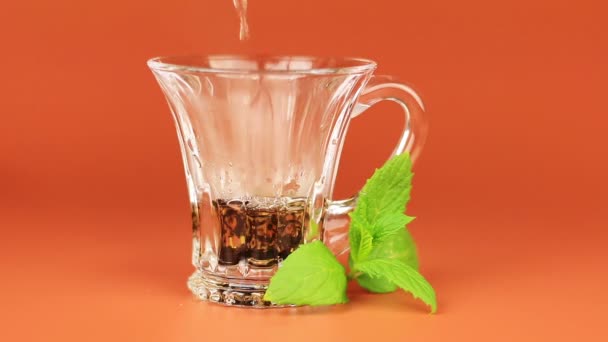 Çay bir cam bardak ve nane yaprağı kahverengi zemin üzerine dökülür. — Stok video