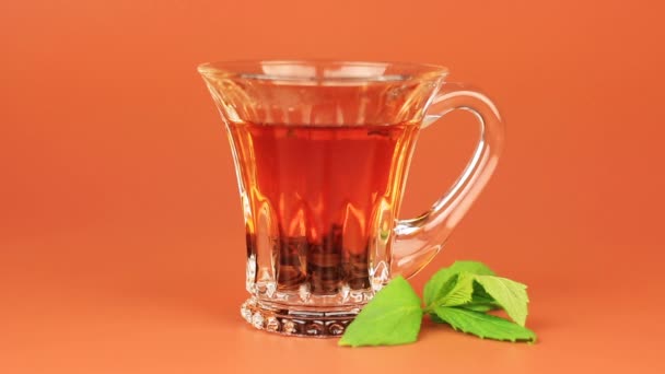 Glas kopp te med mynta blad på brun bakgrund. — Stockvideo