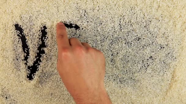 Мужчины рука рисует слово веган на поверхности риса — стоковое видео