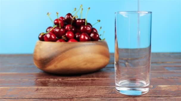 Красный вишневый сок наливают в стакан на деревянный стол и синий фон — стоковое видео
