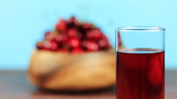 Succo di ciliegia rossa in vetro e ciliegie rosse in ciotola di legno su sfondo blu — Video Stock