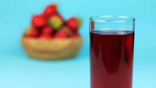 Un vaso de jugo rojo y fresa en un tazón de madera sobre fondo azul — Vídeo de stock