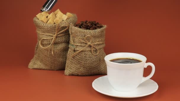 コーヒーは、砂糖と攪拌が配置されます。後ろバーラップ袋のコーヒー豆を立ち次に茶色の背景にバーラップ袋の砂糖 — ストック動画